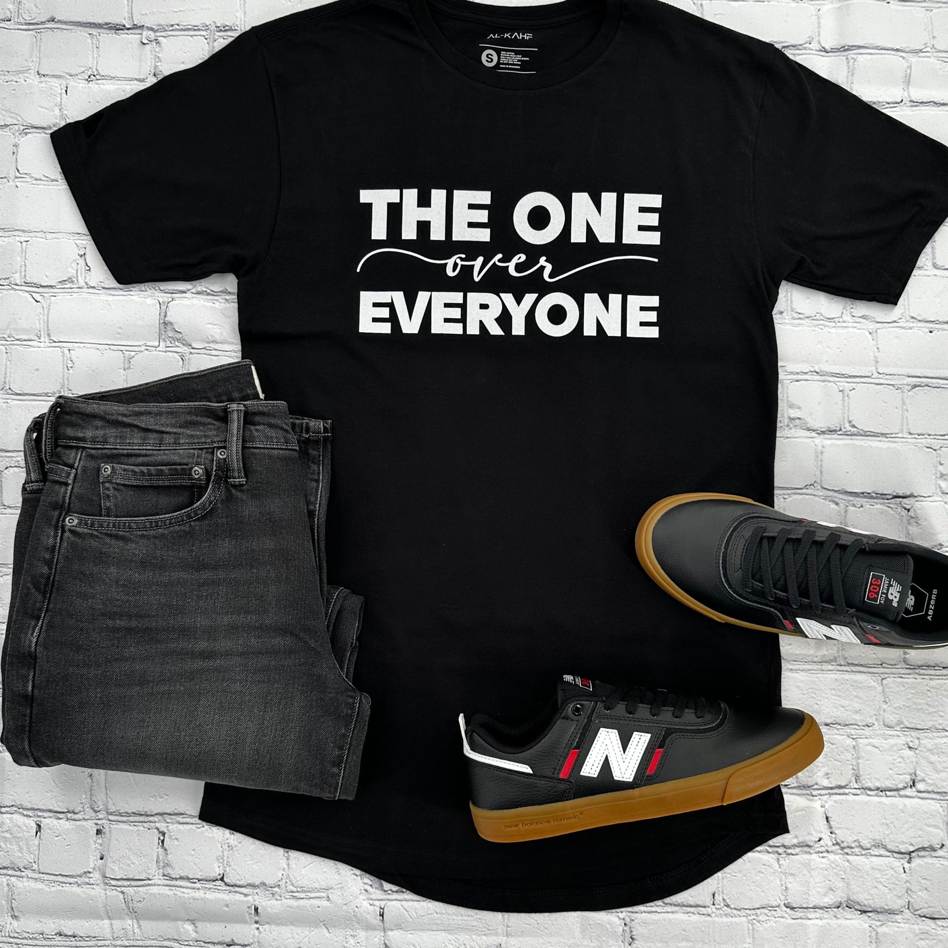 The black AHAD tee pictured alongside gray wash jeans and black New Balance sneakers